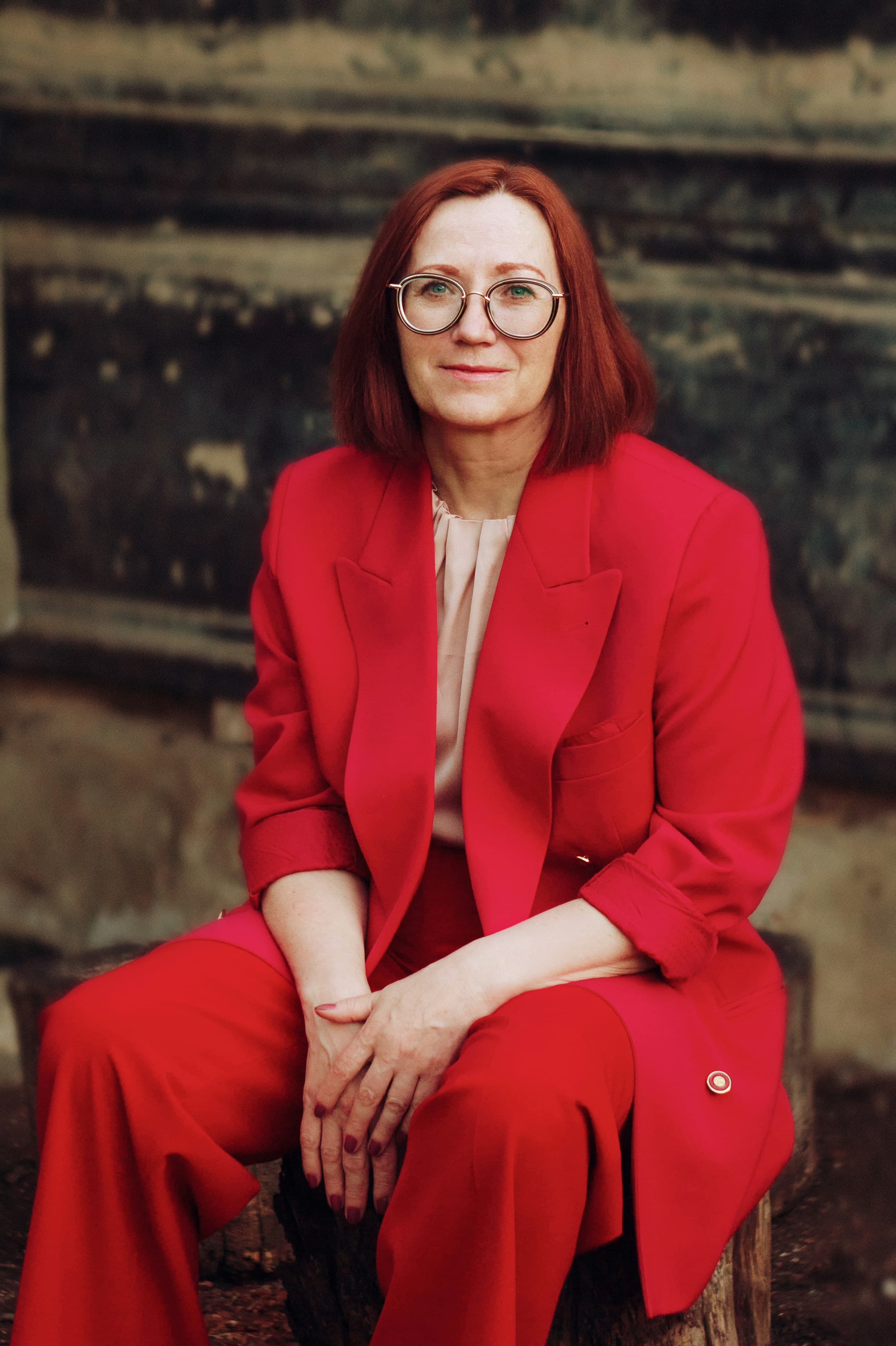 A woman in a red suit, seated and looking directly at the camera